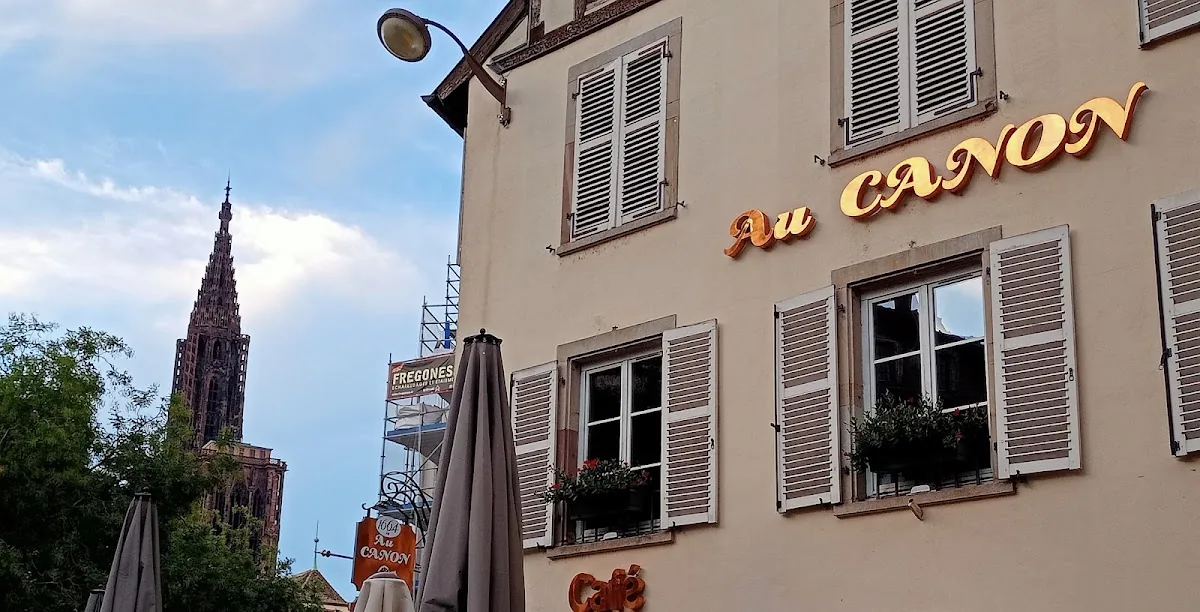 La façade de la brasserie, volets blancs et lettres dorées Au Canon, la cathédrale au fond