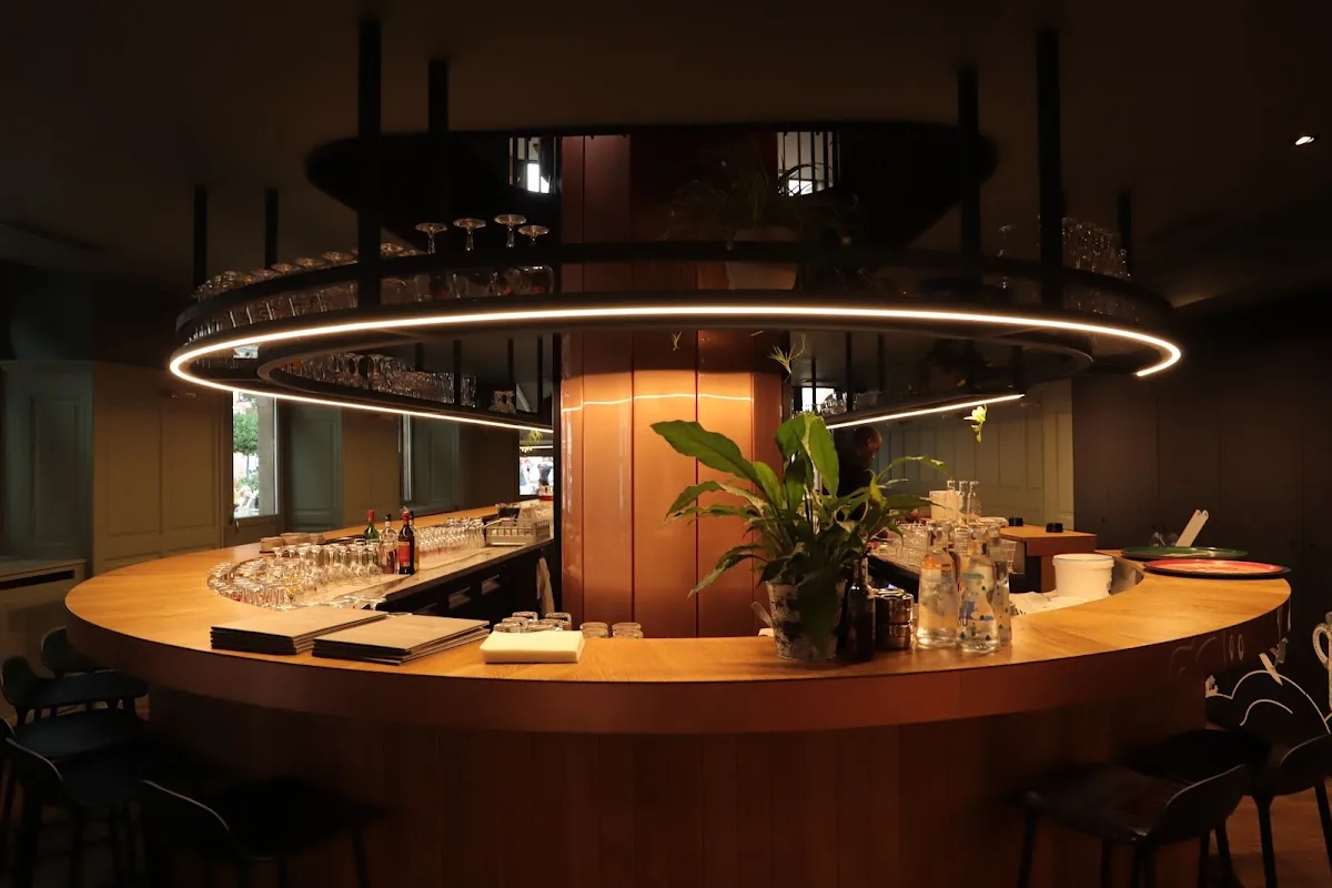 La salle rénovée de la Brasserie Au Canon : comptoir rond en bois sous un anneau de lumière